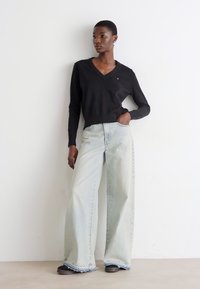 Pulover negru cu guler în V, blugi denim largi de culoare albastră deschisă cu margini desfăcute și pantofi negri. Design simplu cu o croială lejeră.
