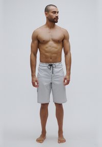 Szürke fürdőnadrág húzózsinóros derékkal, oldalsó zsebbel és kontrasztos varrással. Könnyű, sima anyag, térdig érő szabás.