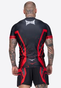 Camiseta atlética de manga corta en negro y rojo con diseños geométricos audaces, degradados y un logo en el cuello. Tela suave y elástica.