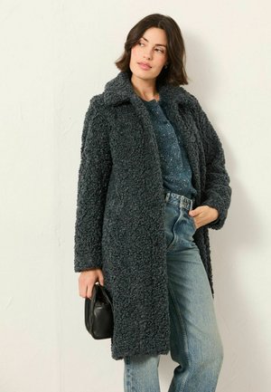 Dunkelgrauer, strukturierter, langer Mantel mit Kragen, Knopfverschluss und oversized Passform, getragen über einem blauen Oberteil und kombiniert mit hochgeschnittenen Jeans.