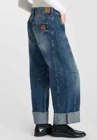 Jeans in denim a gamba larga con un lavaggio blu sbiadito, orli risvoltati e una patta in pelle marrone sulla tasca posteriore, caratterizzati da un design classico delle tasche.