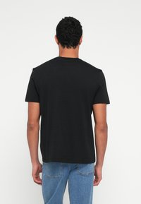 Czarny t-shirt z krótkim rękawem o swobodnym kroju i okrągłym dekolcie, wykonany z miękkiego materiału. Modelka ma na sobie niebieskie dżinsy, pokazując tył koszulki.