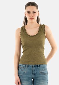 Débardeur vert olive avec un col festonné et un tissu côtelé, associé à un jean bleu clair avec des éléments de décoration.