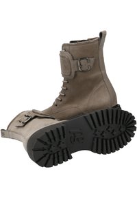 Stivaletto in suede marrone con lacci anteriori, dettaglio con fibbia laterale e suola in gomma nera robusta con profonde scanalature per una migliore aderenza.