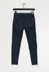 Vaqueros de denim azul oscuro con forma ajustada, diseño de cinco bolsillos y dobladillo desgastado. El material muestra una ligera textura y suavidad.