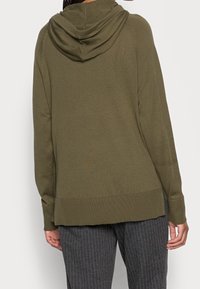 Oliwkowa bluza z kapturem w luźnym kroju, z prążkowanym wykończeniem u dołu i na mankietach, uszyta z miękkiego, teksturowanego materiału dla wygody.