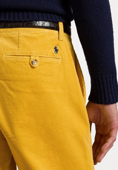 Gula kordfløyelsbyxor med ribbad textur, med knappstängning och en liten blå polo-logotyp ovanför bakfickan.