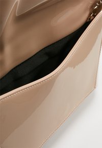 Glansig beige clutch-väska med en mjuk svart tyginsida. Har en smal rektangulär form och sömnadsdetaljer längs kanterna.