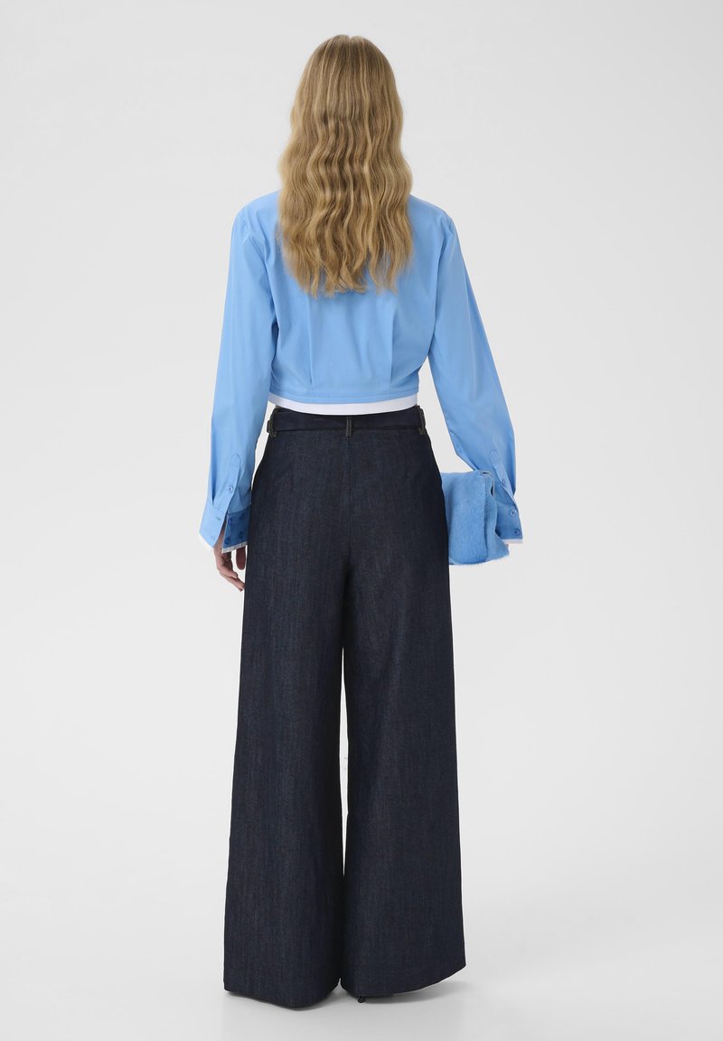 Chemise bleu clair courte à manches longues, associée à un pantalon large en denim foncé et une pochette bleue duveteuse.