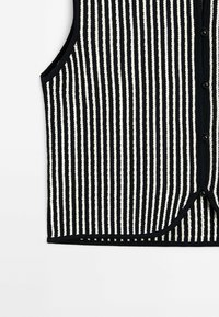 Gilet en tricot rayé verticalement noir et blanc, avec fermeture à boutons sur le devant et design sans manches.