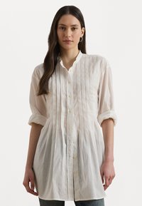 Cămașă albă cu nasturi, cu pliuri verticale, mâneci lungi rulată la manșete, guler mandarin și țesătură ușoară texturată.