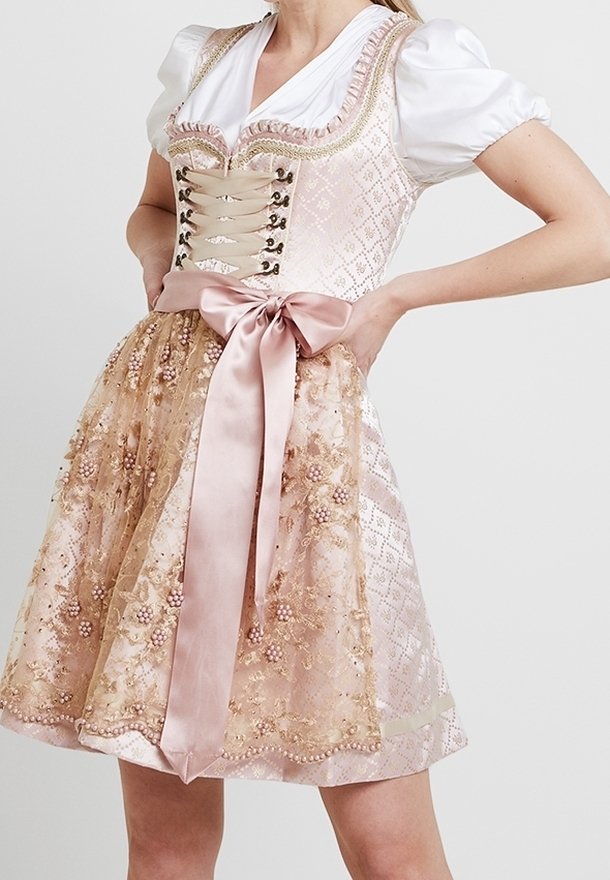 Femme portant une robe traditionnelle rose et or avec des manches bouffantes, un corsage lacé, un tablier en dentelle florale et un grand nœud en satin à la taille.