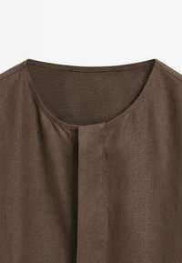 Chemise en lin marron avec encolure ronde et détail de couture verticale centrale sur fond blanc uni.