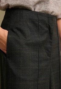Woll-Check-Hosen in Dunkelgrau mit orangefarbenen und braunen Akzenten, mit Seitentaschen und figurschmeichelndem Schnitt. Strukturierter Stoff mit subtiler Schattierung.