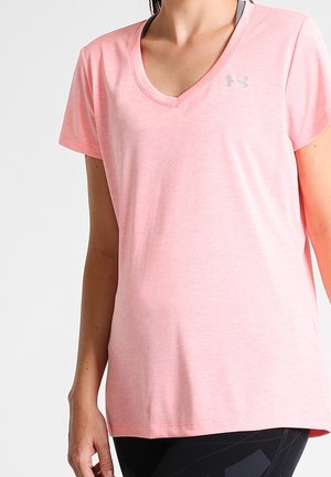 Kobieta nosząca jasnoróżowy sportowy t-shirt z krótkim rękawem i dekoltem w serek, z subtelnym logo na piersi, w połączeniu z czarnymi legginsami.