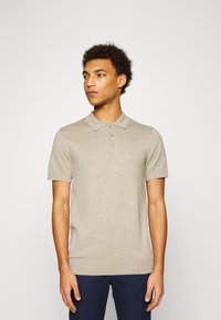 Beige kortärmad pikétröja med krage, fem-knapars knäppning och ribbad nederkant. Tillverkad av ett mjukt, lättstickat tyg.