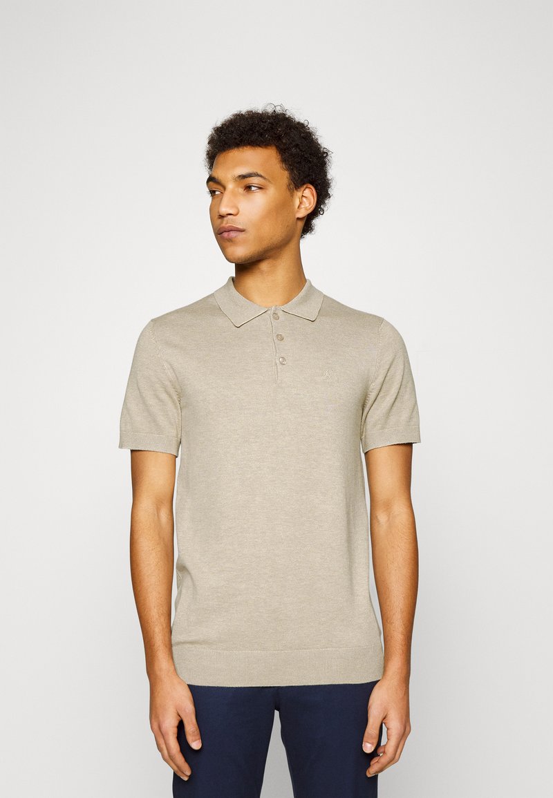 Beige kortärmad pikétröja med krage, fem-knapars knäppning och ribbad nederkant. Tillverkad av ett mjukt, lättstickat tyg.