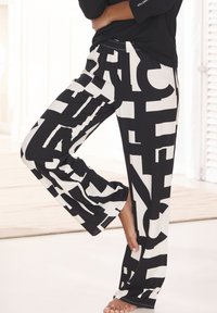 Black and white wide-legged pants with large, bold typographic patterns. Soft material, elastic waistband, and side slits at the hem.