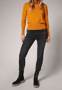 Orange turtleneck sweater, fitted design, paired with slim black jeans. Black ankle boots with thick beige sole. Smooth fabric texture.