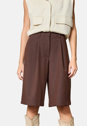 Brune skræddersyede shorts lavet af et letvægtsstof, med et plisseret frontdesign og en midt-lang længde. Båret med en beige ærmeløs top.