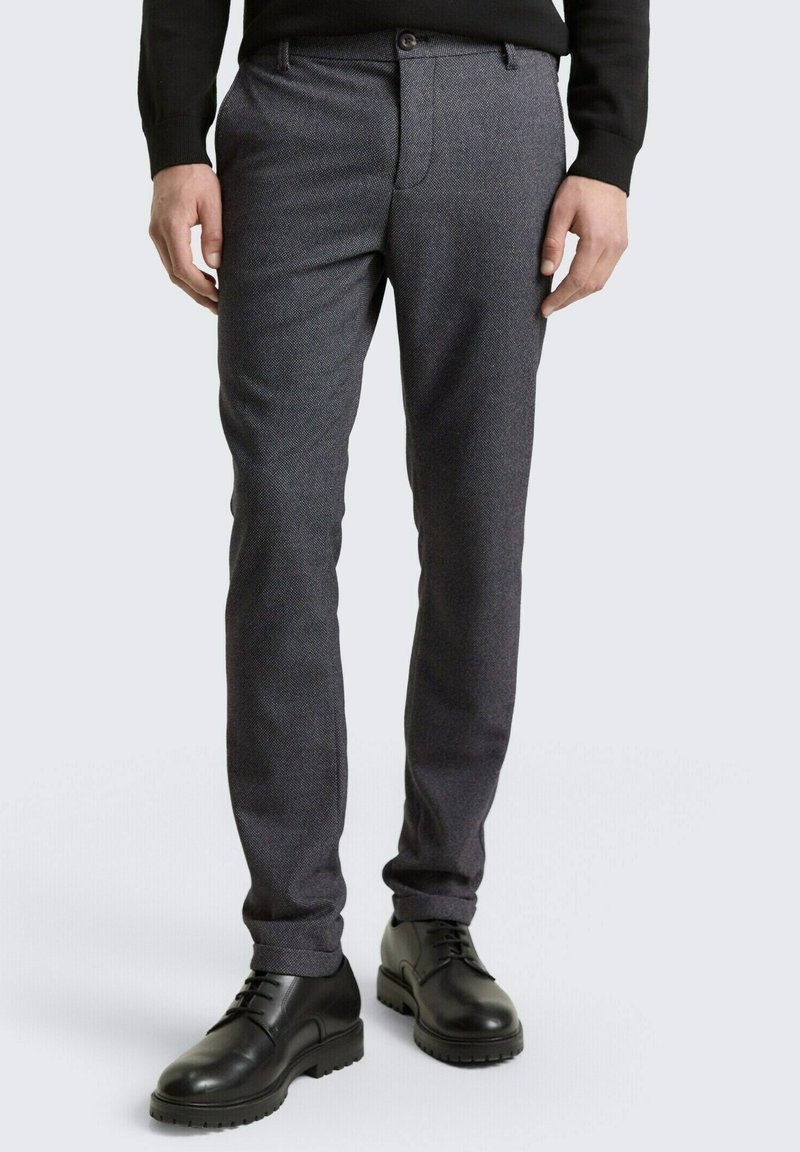 Gray textured dress pants with a slim fit, featuring a flat front and side pockets, paired with black lace-up shoes.