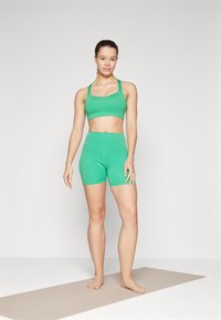 Grønn sports-bh og matchende høytaljede shorts laget av elastisk materiale, med et tettsittende design og glatt tekstur.