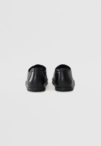 Chaussures en cuir noir avec une texture lisse, un dos arrondi et des coutures autour de la semelle ; conçues pour un enfilage facile.