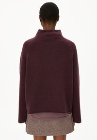 Donkerpaarse, gestructureerde pullover met een hoge kraag, verlaagde schouders en een gelaagd ontwerp. Kenmerkt zich door een contrasterende onderrand en zachte stof.