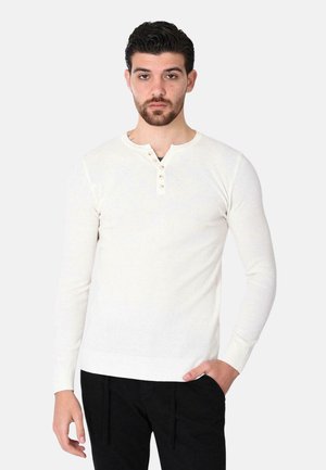 Maglietta henley a maniche lunghe color beige chiaro con collo a giro e patta a tre bottoni, caratterizzata da un motivo a maglia testurizzata e polsini a coste.