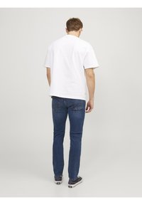 Vitt bomullströja med korta ärmar, i kombination med blå denimjeans. Jeansen har en klassisk passform och tydliga bakfickor.