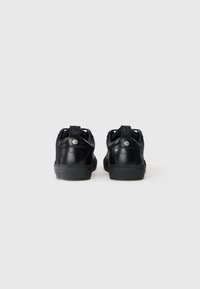 Black leather sneakers with a smooth finish, rubber soles, and subtle branding on the heel. Features reinforced stitching and eyelets.