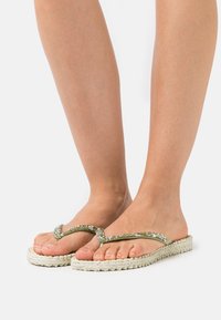 Infradito verdi con una parte superiore luccicante e suola piatta beige intrecciata, caratterizzate da una finitura testurizzata e un design curvo.