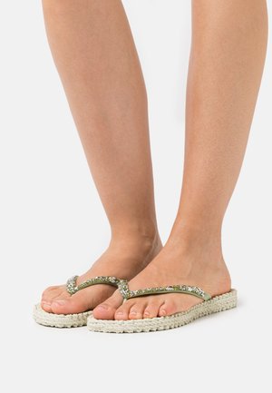 Infradito verdi con una parte superiore luccicante e suola piatta beige intrecciata, caratterizzate da una finitura testurizzata e un design curvo.