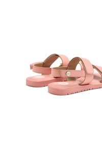 Sandalias rosas con suela plana, dos correas y un acento de hebilla. Elaboradas con un material suave y con una suela texturizada para mayor agarre.