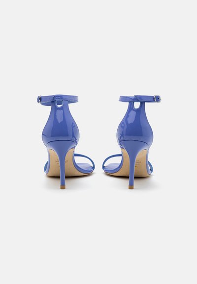 Sandales à talons hauts en cobalt brillant avec des bretelles autour de la cheville et des talons aiguilles fins, vues de l'arrière sur un fond blanc.