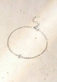 Bracelet en chaîne argentée avec un fermoir réglable, présentant un petit accent décoratif avec des embellissements transparents au centre.