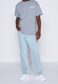 Grå t-shirt i bomull med rund halsringning och korta ärmar, kombinerad med ljusblå baggy jeans och vita sneakers.