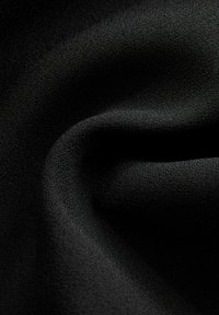 Tissu noir texturé avec un pli doux et lisse créant des courbes et des ombres délicates à la surface.