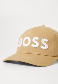 Sötét színű baseball sapka, fehér hímzett "BOSS" logóval, struktúrált formával és texturált anyaggal, ívelt szárral.
