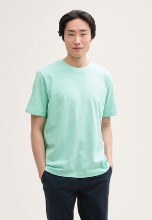 Mintgroene katoenen T-shirt met korte mouwen, ronde halslijn en een relaxte pasvorm, gecombineerd met donkerblauwe broek. Gladde textuur, minimalistisch ontwerp.