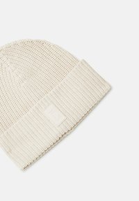 Skręcany kremowy beanie z prążkowanym wywinięciem kufra i małą, wytłaczaną metką z logo z boku. Teksturowany materiał nadaje mu przytulny wygląd.
