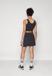 Fekete sportos crop top és plissé szoknya fehér oldalsávokkal, fekete futócipőkkel és fehér zoknikkal, fekete csíkokkal.