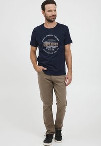 Mørkeblå t-shirt med rund halsudskæring, prydet med et grafisk print i beige og hvid. Sammen med lysebrune chinos og sorte sneakers.