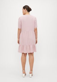 Φωτεινό ροζ φόρεμα με κοντά φουσκωτά μανίκια, στρογγυλή λαιμόκοψη και φούστα με στιλ ραμμένος βολάν σε επίπεδες σειρές. Φτιαγμένο από μαλακό ύφασμα με απαλή υφή.