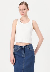Biely rebrovaný crop top so širokými ramienkami, skombinovaný s džínsovou sukňou s vysokým pásom. Materiál je štruktúrovaný a sukňa má predný rozparok.