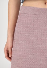 Falda tejida en rosa con un acabado texturizado. Presenta una cinturilla suave y un diseño ajustado, que muestra variaciones sutiles en el color.
