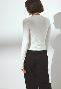 Haut blanc à manches longues au design ajusté avec une texture lisse, associé à un jean noir taille haute avec poches arrière.