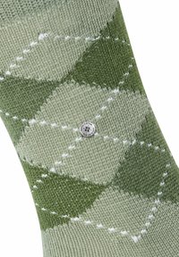Calze argyle verdi con diverse sfumature di verde e accenti bianchi, realizzate in tessuto a maglia testurizzato, e un piccolo dettaglio del logo circolare.