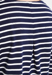 Navy blue ja valge triibuline kangas, millel on volditud detail taga, pehme tekstuur ja ümar kaelus. Nähtavad õmblemise aktsendid.