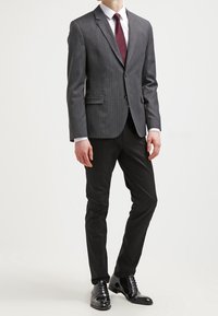 Grau gestreifter Anzugjacke mit schwarzen Hosen, weißem Hemd und burgundfarbenem Krawatte. Polierte schwarze Schuhe. Maßgeschneiderte Passform.